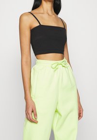 Svart croppad tanktopp med tunna axelband, tillsammans med högmidjade neongröna sweatpants med elastisk midja och sidofickor.