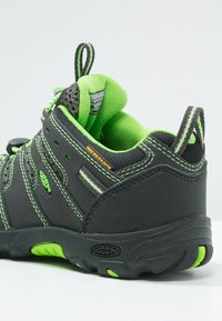 Mustat ja vihreät vedenpitävät kengät, joissa on teksturoitu pinta, vahvistetut saumat, pehmustettu nilkkapanta ja kestävä kumipohja, jossa on pitävää koristetta.