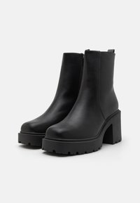 Botines de cuero negro hasta el tobillo con una plataforma y tacón robustos, que presentan un cierre lateral y una textura suave. Sin patrones ni acentos visibles.