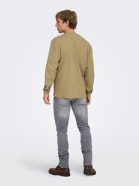 Pull-over en coton vert olive à manches longues avec un motif texturé, assorti à un jean gris slim et des bottes en cuir marron.