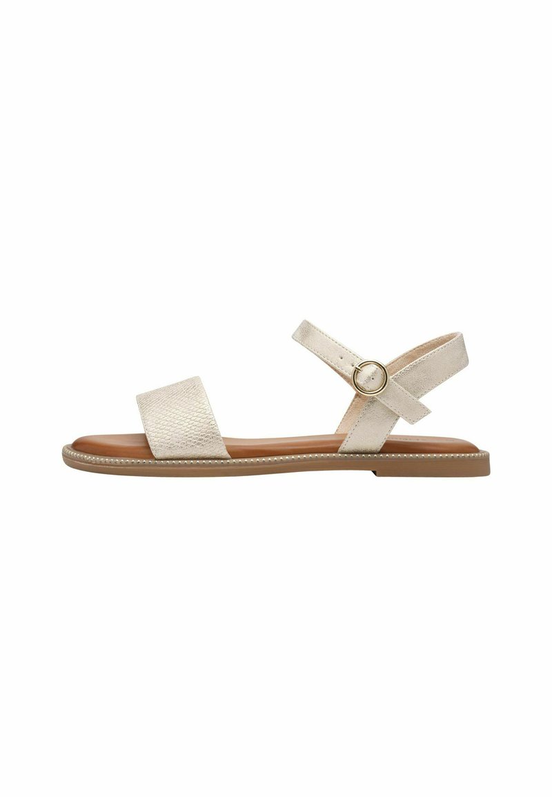 Des sandales beige clair présentent un dessus texturé avec deux larges sangles et une boucle circulaire, reposant sur une semelle plate couleur tan avec une bordure subtile.
