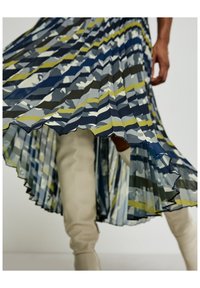 Monivärinen taitettujen laskosten hame, jossa maastokuvio tummansinisillä, vihreillä ja harmailla sävyillä; aaltoileva helma ja kevyt kangas.