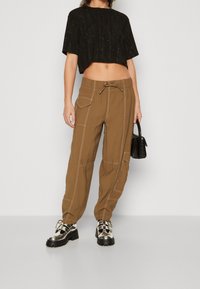 Černý cropped top s texturovanou tkaninou a jiskřícími detaily, zkombinovaný s hnědými cargo kalhotami s několika kapsami a kontrastním šitím. Stříbrné boty.