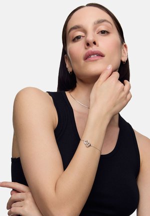 Srebrna bransoletka łańcuszkowa o splocie, noszona na nadgarstku. Gładka faktura, minimalistyczny styl. Czarny top na ramiączkach w tle.