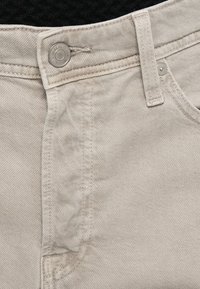 Light beige denim jeans featuring a metal button closure, tonal stitching, and a smooth texture with a slight stretch.