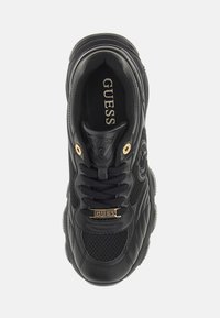 Black GUESS sneaker with mesh and leather details, gold eyelets, branded lace tag, and logo patch on the side, viewed from above.