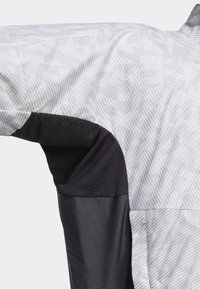 Lekka kurtka z białym i szarym paskowanym wzorem, czarnymi siateczkowymi wstawkami oraz gładkim czarnym materiałem na tułowie i rękawach.