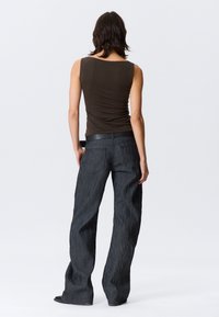 Παντελόνι τζιν με φαρδιά μπατζάκια σε σκούρο γκρι με υφή και πίσω τσέπες, σε συνδυασμό με εφαρμοστή καφέ αμάνικη μπλούζα. Το ντύσιμο είναι μινιμαλιστικό και σύγχρονο.