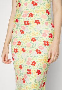 Vestido floral em tecido amarelo claro com padrões vermelhos, cor-de-rosa e verdes. Design justo com uma textura suave.