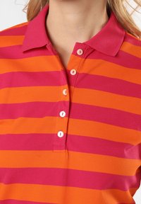 Pruhované polo tričko s širokými vodorovnými oranžovými a růžovými pruhy, s límečkem a knoflíkovou légou vyrobeným z bavlněné tkaniny.