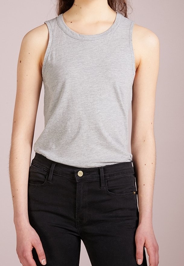 Haut sans manches en coton gris avec un col rond, associé à un jean noir ajusté et un détail de bouton doré. Texture de tissu lisse.