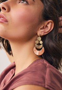 Gold-tone earrings with a textured circular top and a layered fan design featuring blush and coral fabric accents.