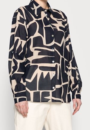 Chemise à boutons à manches longues à motifs abstraits noirs et beiges, portée avec un pantalon blanc cassé, montrée du cou aux hanches.