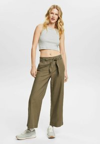 Grønne vide bukser med bånd i taljen, lette materialer, forlommer og opkrøllede kanter, parret med en grå cropped tanktop og grå sneakers.