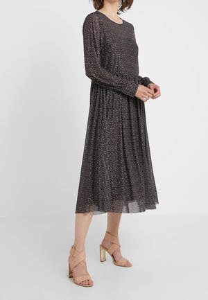 Robe noire à manches longues avec un motif floral et une taille froncée, fabriquée en tissu léger. Associée à des sandales à talons beiges avec des accents dorés.