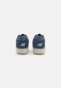 Un paio di sneakers New Balance blu navy viste da dietro, con tessuto testurizzato e suole intermedie bianche con suole esterne beige.