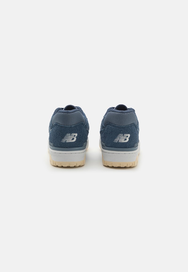 Un paio di sneakers New Balance blu navy viste da dietro, con tessuto testurizzato e suole intermedie bianche con suole esterne beige.