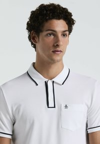 Weißes Poloshirt aus strukturiertem Stoff mit schwarzem Kragen und Knopfleiste. Verfügt über eine Brusttasche mit Logodetail.