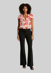 Chemise à boutons rouge à motifs floraux associée à un pantalon évasé noir. La chemise a un col et des manches courtes ; le pantalon possède des poches avant avec des accents en métal.