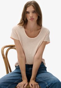 Lyserød T-shirt med korte ærmer og rund hals, blød tekstur, løs pasform, kombineret med blå jeans med høj talje.