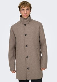 Manteau marron en mélange de laine avec un col montant, cinq boutons noirs, poches latérales et une coupe droite. Texture douce avec une finition lisse.