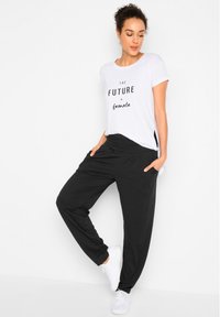 Maglietta bianca con testo nero "IL FUTURO è femminile" abbinata a pantaloni neri larghi con tasche e scarpe da ginnastica bianche.