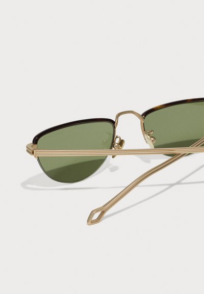 Gold metal sunglasses with oval green lenses. Slim frame and arms, featuring a geometric-shaped end tip detail.