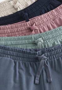 Cinco pares de pantalones cortos de deporte en una disposición apilada: beige, azul marino, rosa, verde y azul oscuro; todos cuentan con cinturas elásticas y cordones trenzados.