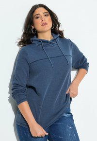 Felpa con cappuccio blu caratterizzata da un motivo a costine testurizzato, chiusura con coulisse e maniche lunghe, abbinata a jeans blu strappati.
