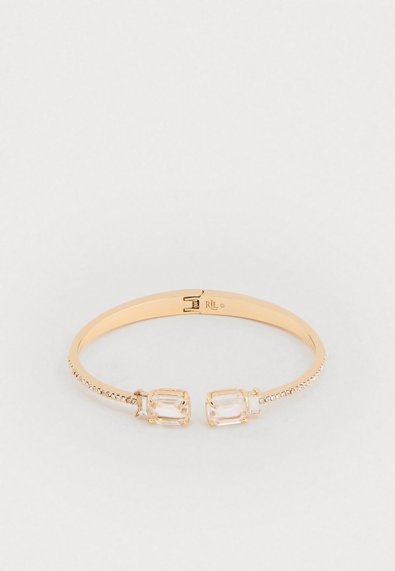 Arany színű bangle karkötő, két téglalap alakú átlátszó kristállyal, valamint egy texturált szalaggal, amely az egyik oldalon kis átlátszó gyöngyökkel van díszítve.