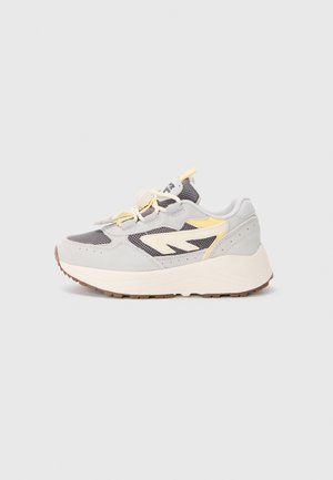Baskets de sport grises et jaunes avec une tige en mesh, des accents en daim, une épaisse semelle blanche et une semelle extérieure en caoutchouc texturé. Comprend des lacets et un marquage.