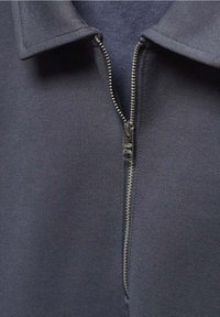 Sudadera de cremallera gris oscuro con cuello, que presenta una cremallera metálica y una textura suave, destacando un diseño minimalista y detalles funcionales.