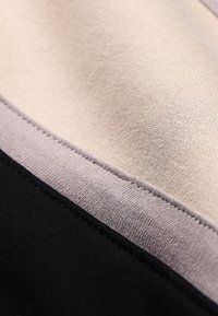 Υφασμα με υφή σε μπεζ, γκρι και μαύρα τμήματα, με λεία, ματ φινιρίσματα και ακριβείς ραφές κατά μήκος των άκρων.