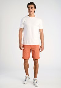 T-shirt bianca a maniche corte, pantaloni corti arancioni a scacchi con risvolti, e scarpe da ginnastica bianche con lacci colorati. Design minimalista.