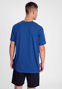 Camiseta de algodón azul con mangas cortas y escote redondo, que presenta una textura suave y un ajuste relajado, combinada con pantalones cortos negros.