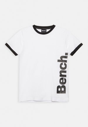T-shirt blanc à manches courtes avec col et bords de manches noirs, arborant le logo vertical noir "Bench" sur le côté droit.