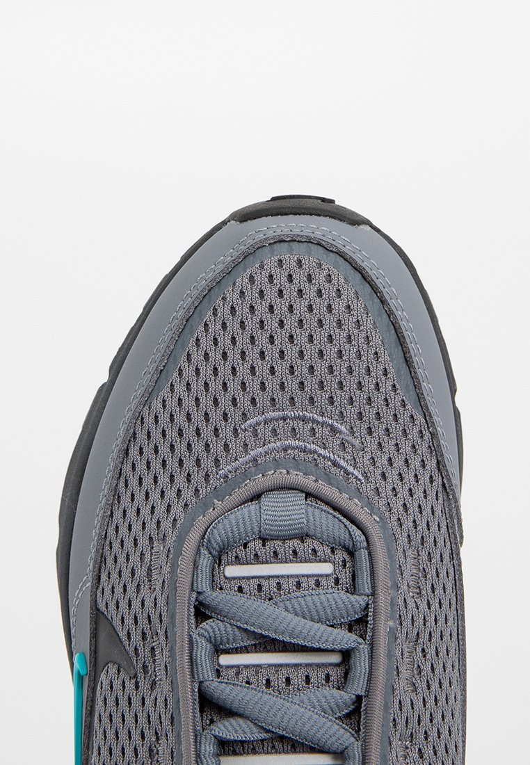Zapatilla deportiva gris con parte superior de malla, suela de goma y acentos en teal contrastantes. Presenta cordones planos y área de puntera reforzada.