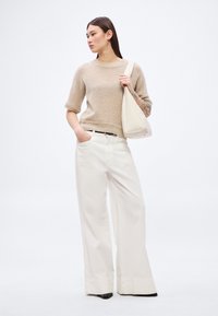 Šviesiai rudas trumpomis rankovėmis megztinis, laisvos baltos kelnės ir balta peties rankinė. Kelnės iki grindų, su lygiu audiniu ir subtiliomis siūlėmis.