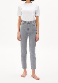 Jeans in denim grigio chiaro a vita alta, con un taglio slim. Presentano cinque tasche, passanti per cintura e una texture sbiadita. Indossati con una maglietta bianca.