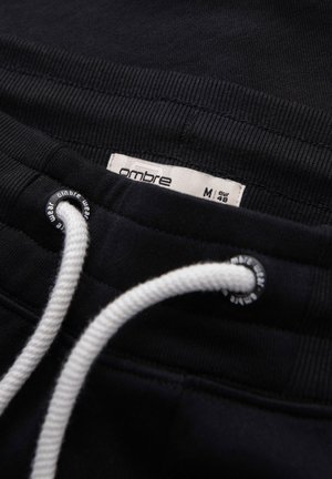 Schwarzer elastischer Hosenbund mit weißem Kordelzug und sichtbarem Größenetikett „ombre M eur 45“ innen.