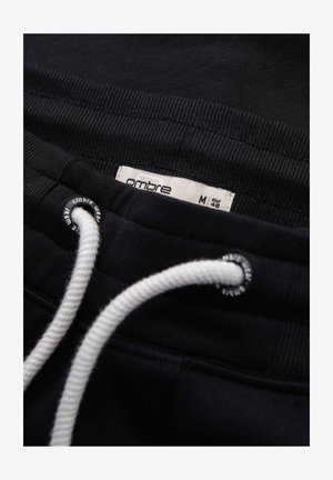 Czarna elastyczna talia spodni z białym sznurkiem i widoczną metką rozmiaru "ombre M eur 45" wewnątrz.