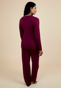 Ensemble de détente bourgogne comprenant un haut à manches longues avec un col rond et un pantalon à jambes larges avec un bord en dentelle. Texture douce et lisse.