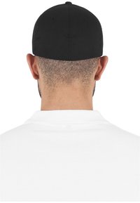 Cappellino nero con una texture di tessuto liscia, forma arrotondata e dettagli cuciti sulla parte superiore. Indossato al contrario, rivela un colletto bianco di polo.