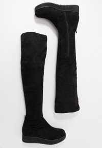 Czarne kozaki ponadkolanowe wykonane z miękkiego zamszu, wyposażone w klinowy obcas, boczny zamek błyskawiczny oraz dopasowany krój sięgający ponad kolano.