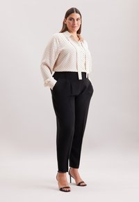 Witte blouse met zwarte stippen, hoge zwarte broek, en zwarte sandaaltjes met bandjes. Gladde stof, nauwkeurige pasvorm, net ontwerp.