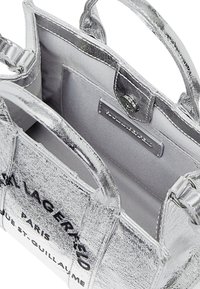 Silver metallic handbag with short handles and a zip closure. Spacious interior features a fabric lining and a small brand label.