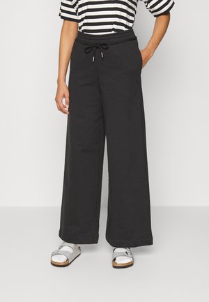 Zwarte wijde trainingsbroek met een elastische tailleband, trekkoorddetail en zijzakken. Draagt een gestreept shirt en zilveren sandalen.