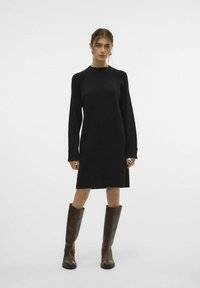 Schwarzes Langarmkleid mit rundem Halsausschnitt, lockerer Passform und gerippten Texturen an den Bündchen, kombiniert mit knielangen braunen Lederstiefeln.