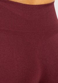 Bordowe legginsy o wysokim stanie, prążkowane, z gładką teksturą i wzmocnioną talią. Subtelny trójkątny wzór z przodu przechodzi płynnie.