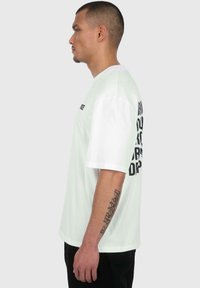 Weißes T-Shirt mit kurzen Ärmeln und schwarzem Text auf dem Rücken und der linken Brust, aus Baumwolle gefertigt, mit lockerer Passform und Rundhalsausschnitt.